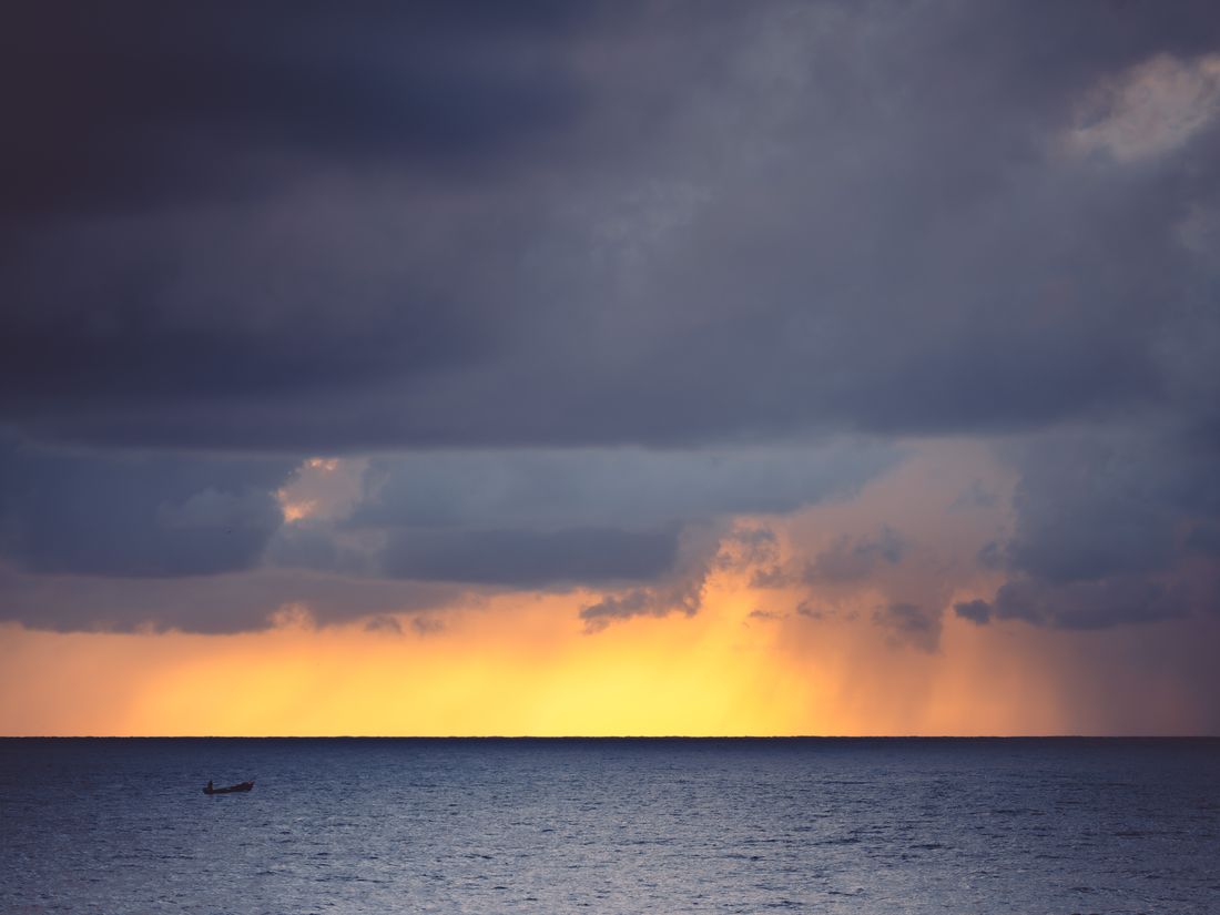 Storm clouds parting to golden light over calm water, with a lone fishing boat on the horizon